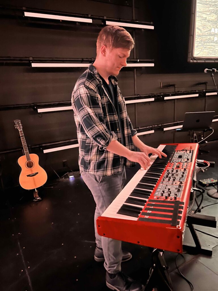 Brady Wetz playing a red keyboard on stage at church.